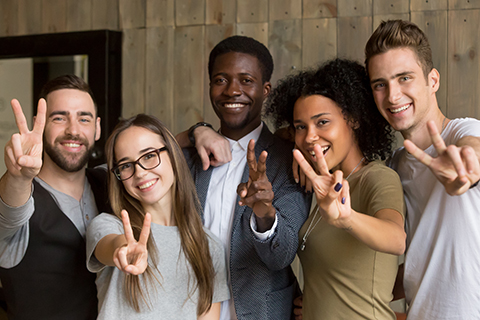 This is a stock photo. A diverse group of adults making a peace sign with their fingers.