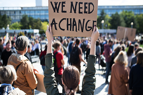 A close up photo of a sign at a climate change protest. The sign reads, "We Need A Change."